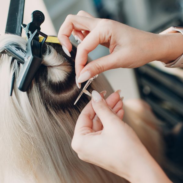 Hands applying K-tip hair extensions with precision, showcasing keratin bond technique for natural movement and blend at Refined Beauty Boutique.