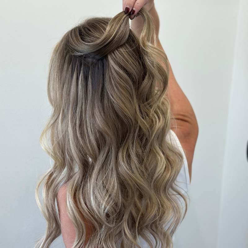 Woman showcasing styled hair with K-Tip extensions, featuring soft waves and a half-up hairstyle, demonstrating versatility for various looks.